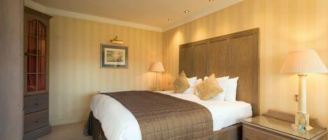 A neatly arranged bedroom with a large bed, a bedside table with a lamp, a wooden wardrobe, and a framed picture on the wall.