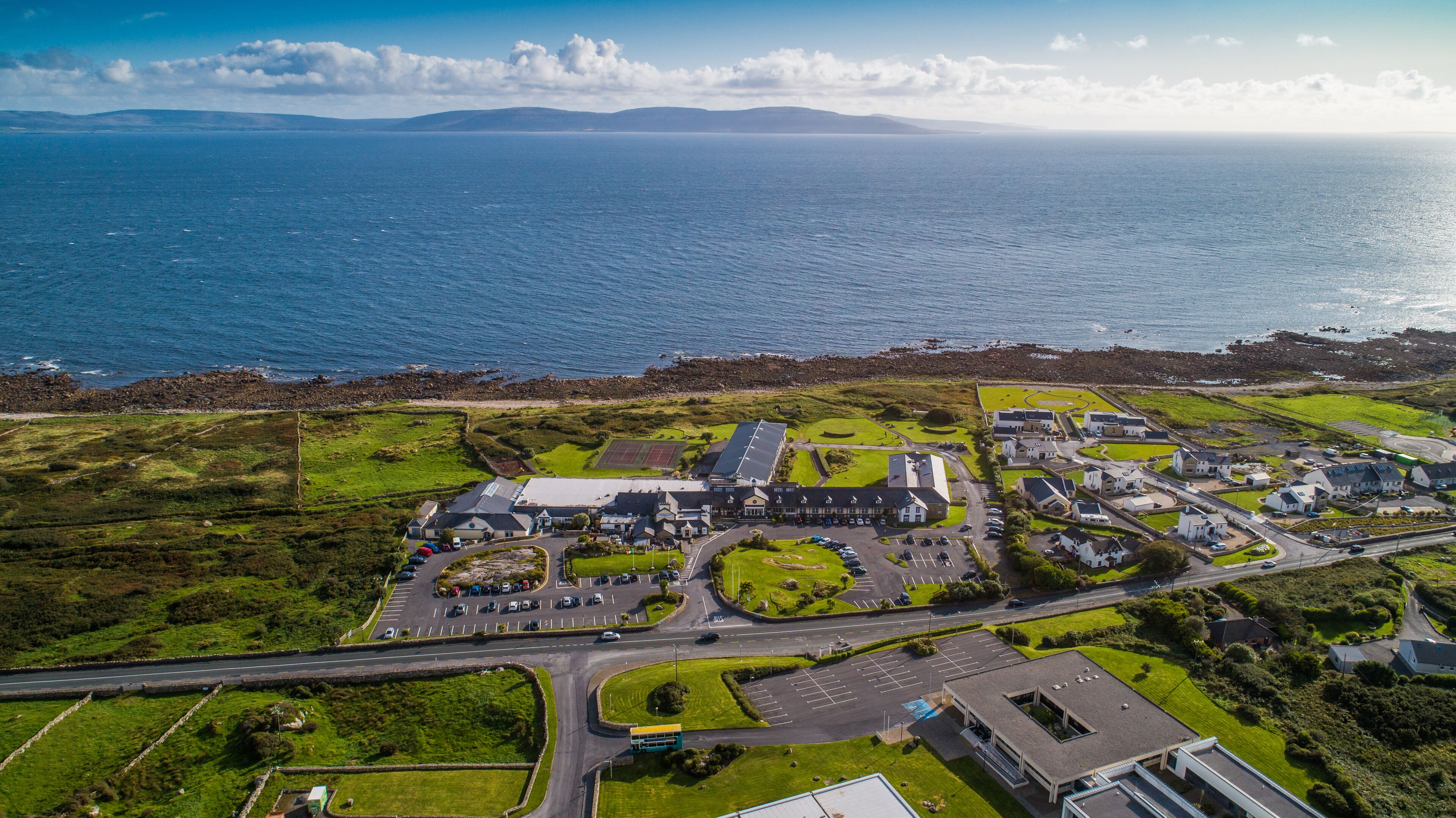 An aerial view of a coastal town with a marina, green spaces, and buildings with parking lots.
