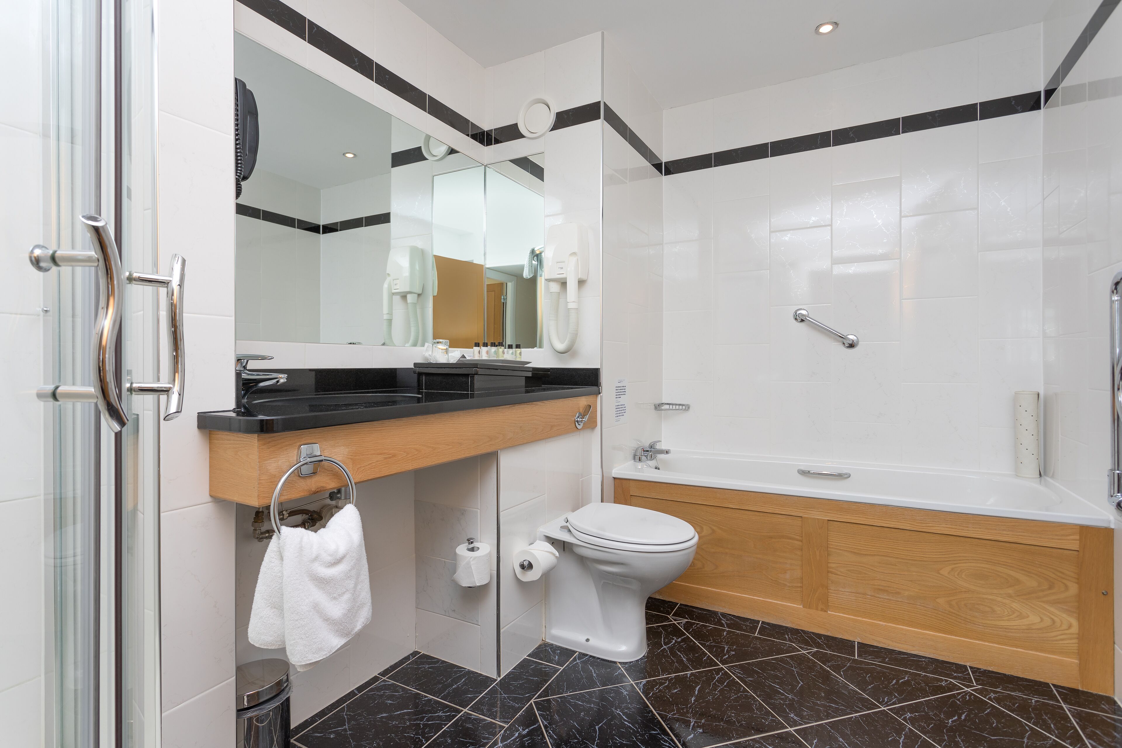 Une salle de bain moderne avec une douche à parois de verre, un meuble-lavabo en bois, des toilettes blanches et une baignoire blanche.