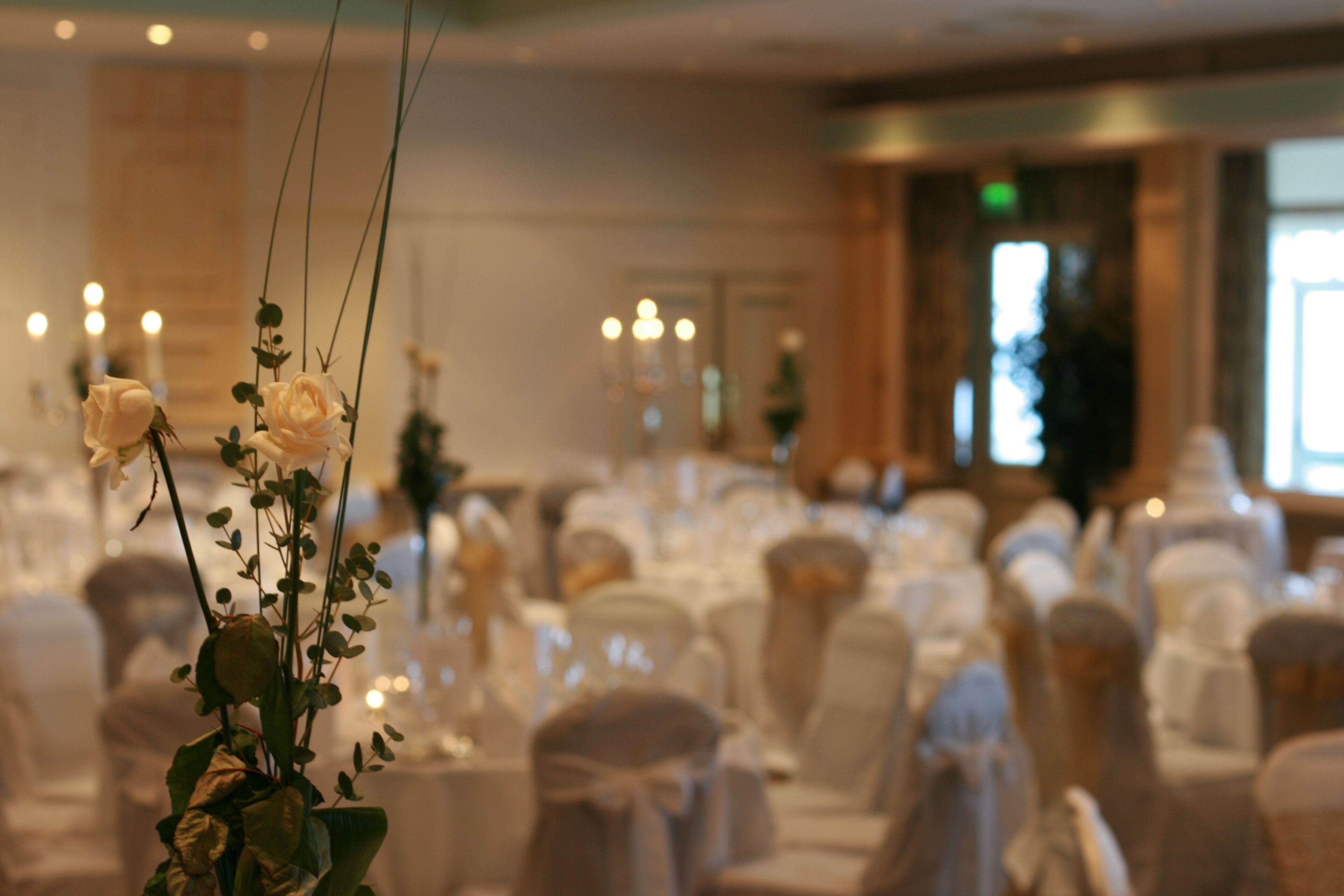 A banquet hall with round tables set for a formal event, adorned with white tablecloths and floral centerpieces.