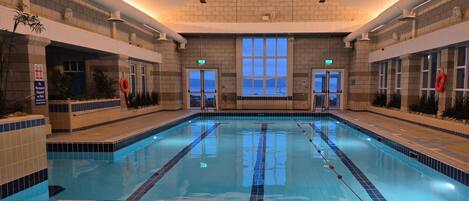 An indoor swimming pool with clear lanes, a tiled floor, and a view of the outside through large windows.