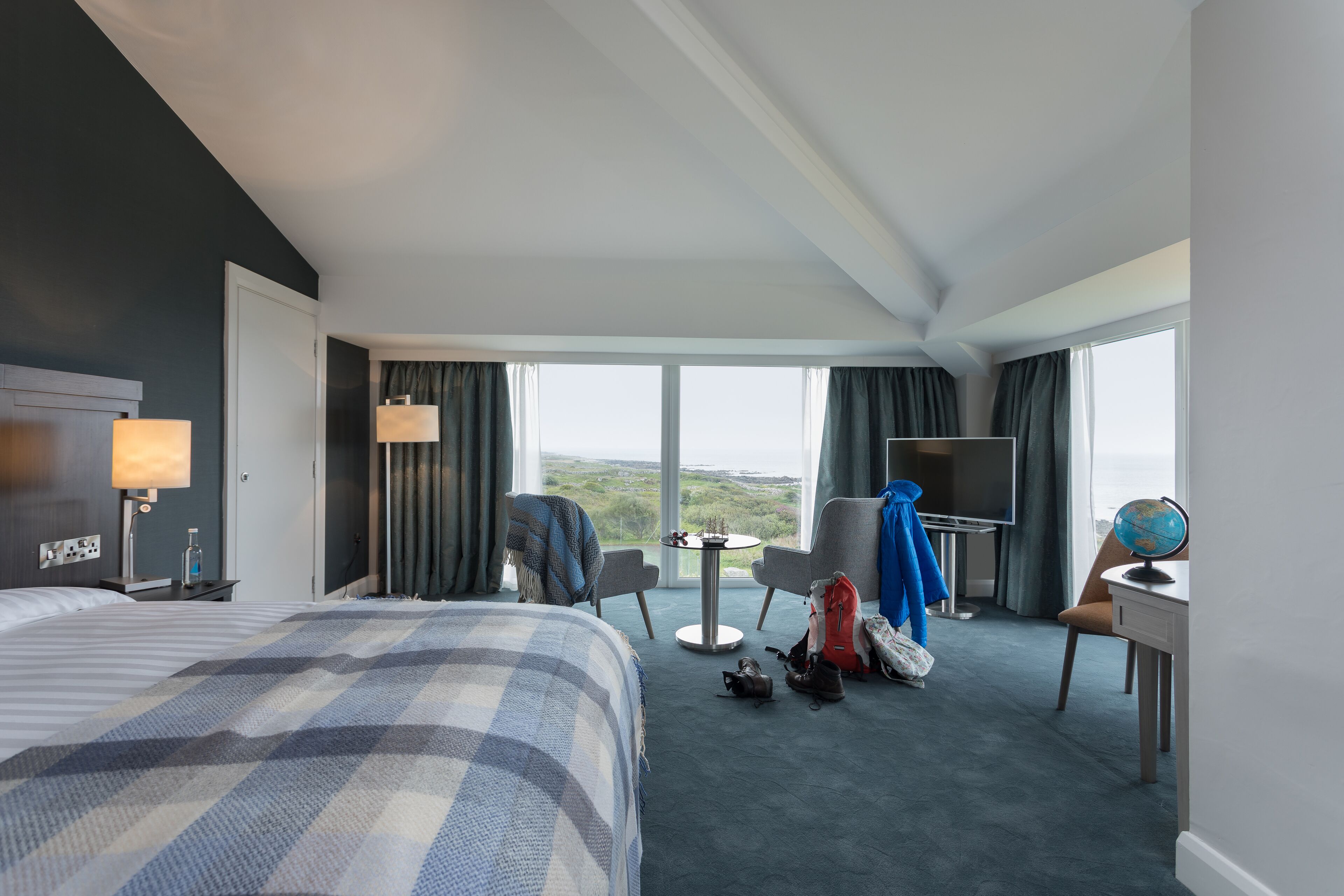 Une chambre d’hôtel avec un grand lit, un bureau avec un globe terrestre, une chaise, une télévision et une vue sur l’extérieur.