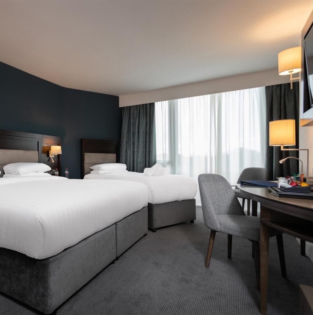 A hotel room with two beds, a desk, and a chair.