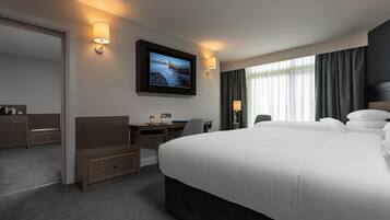 A hotel room with a large bed, a desk with a chair, a television mounted on the wall, and a window with curtains.