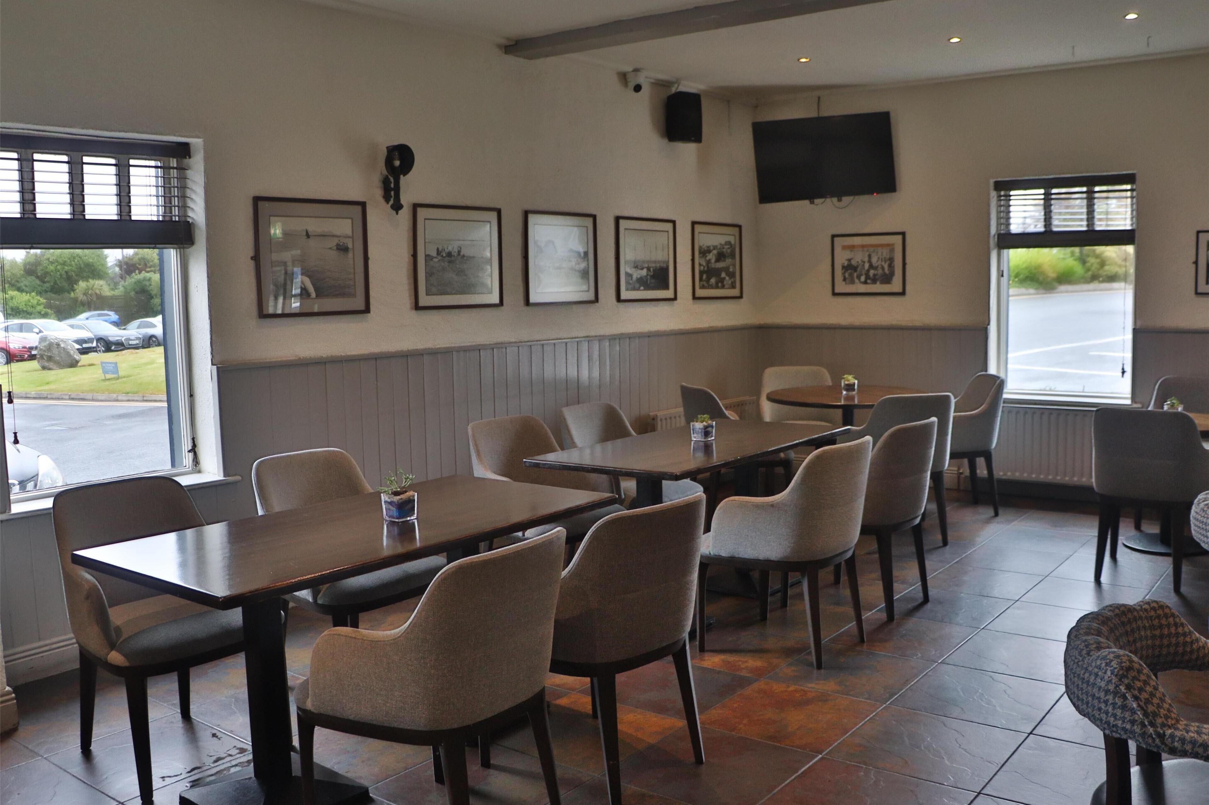 A restaurant with multiple tables and chairs, framed pictures on the wall, and a television mounted on the wall.