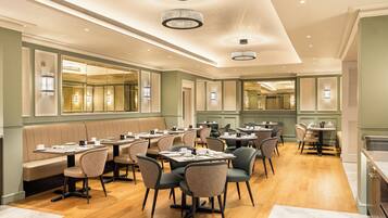 A spacious dining area with multiple tables and booths, featuring a wooden floor and elegant lighting fixtures.