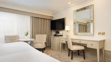 A hotel room with a bed, a desk, two chairs, a television, a mirror, and a small table with a vase of flowers.