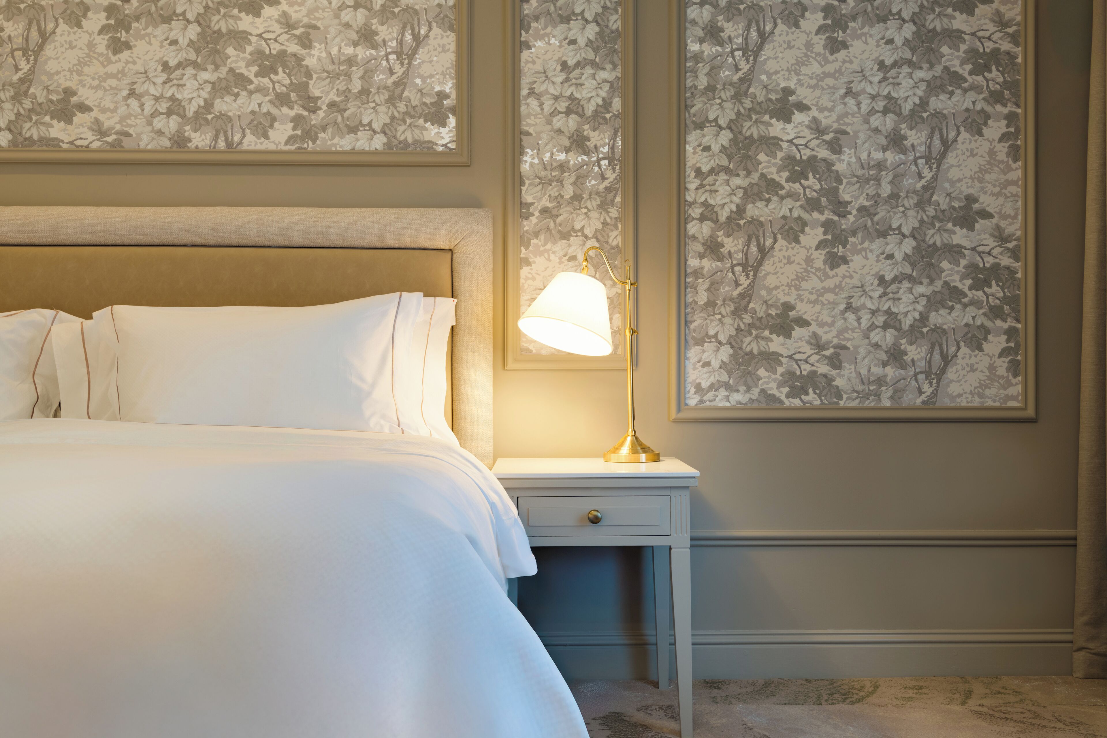 A neatly made bed with white linens, a bedside lamp, and a small drawer.