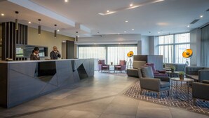 Un moderno vestíbulo de hotel con una recepción, zona de estar y ventanas amplias.