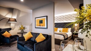 Une chambre d’hôtel moderne avec un canapé noir, deux fauteuils, une petite table ronde et un lit avec une tête de lit.
