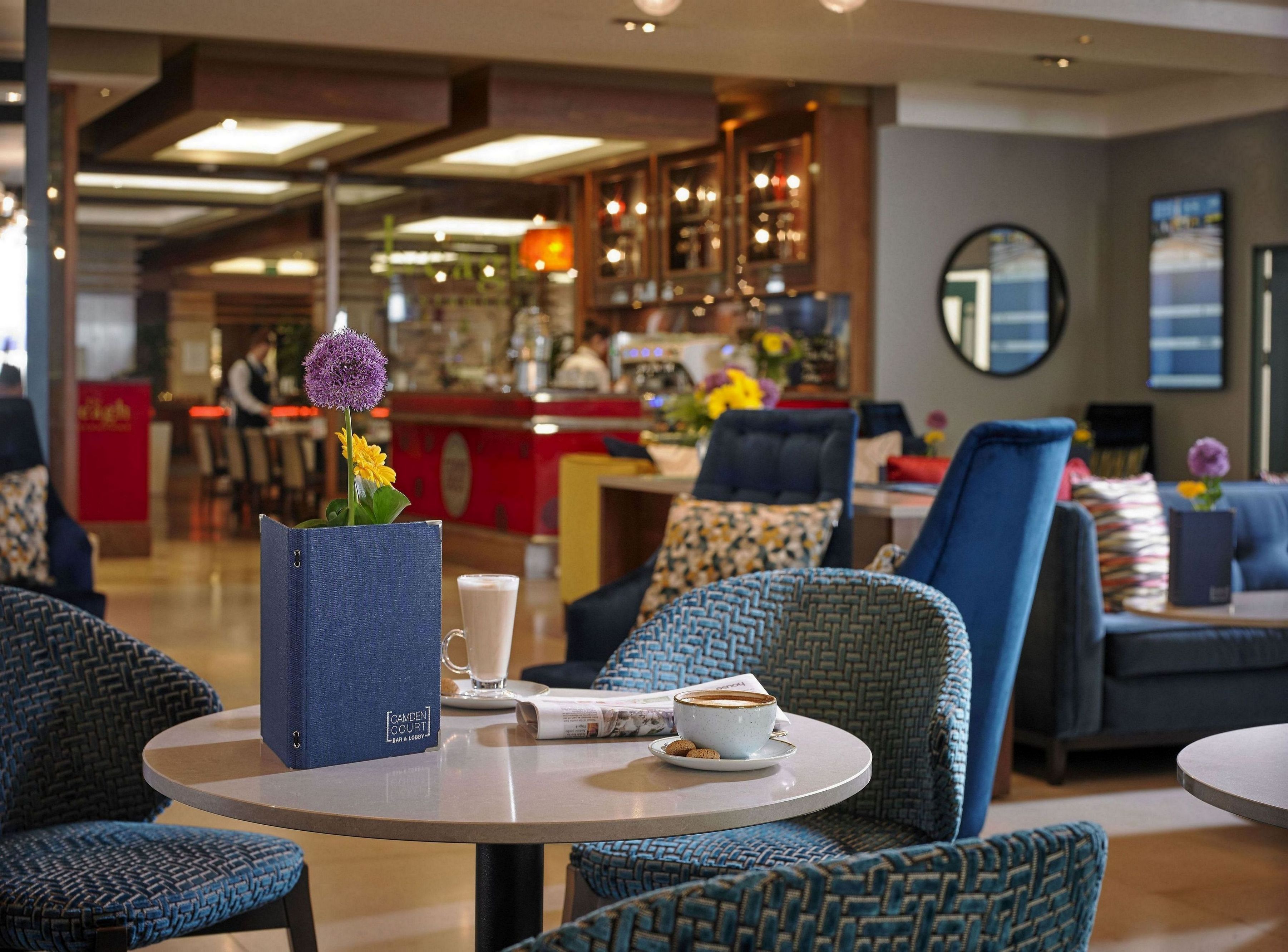 A modern lounge area with round tables, comfortable seating, and a bar in the background.