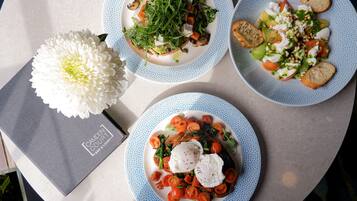 Drei Teller Essen auf einem Tisch, mit einer weißen Blume und einer grauen Tasche.