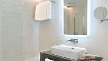 Ένα σύγχρονο μπάνιο με λευκό νιπτήρα, έναν μεγάλο καθρέφτη και μια περιοχή με ντους.