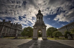 A historic building with a prominent archway and a tower, surrounded by trees and other structures.