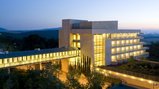 A modern hotel with a glass facade, multiple balconies, and a covered walkway.