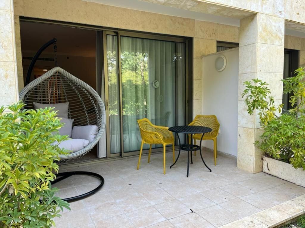 Une terrasse avec un fauteuil en osier, deux chaises jaunes, une petite table et des plantes en pot.