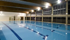 An indoor swimming pool with clear lanes, large windows, and a high ceiling.