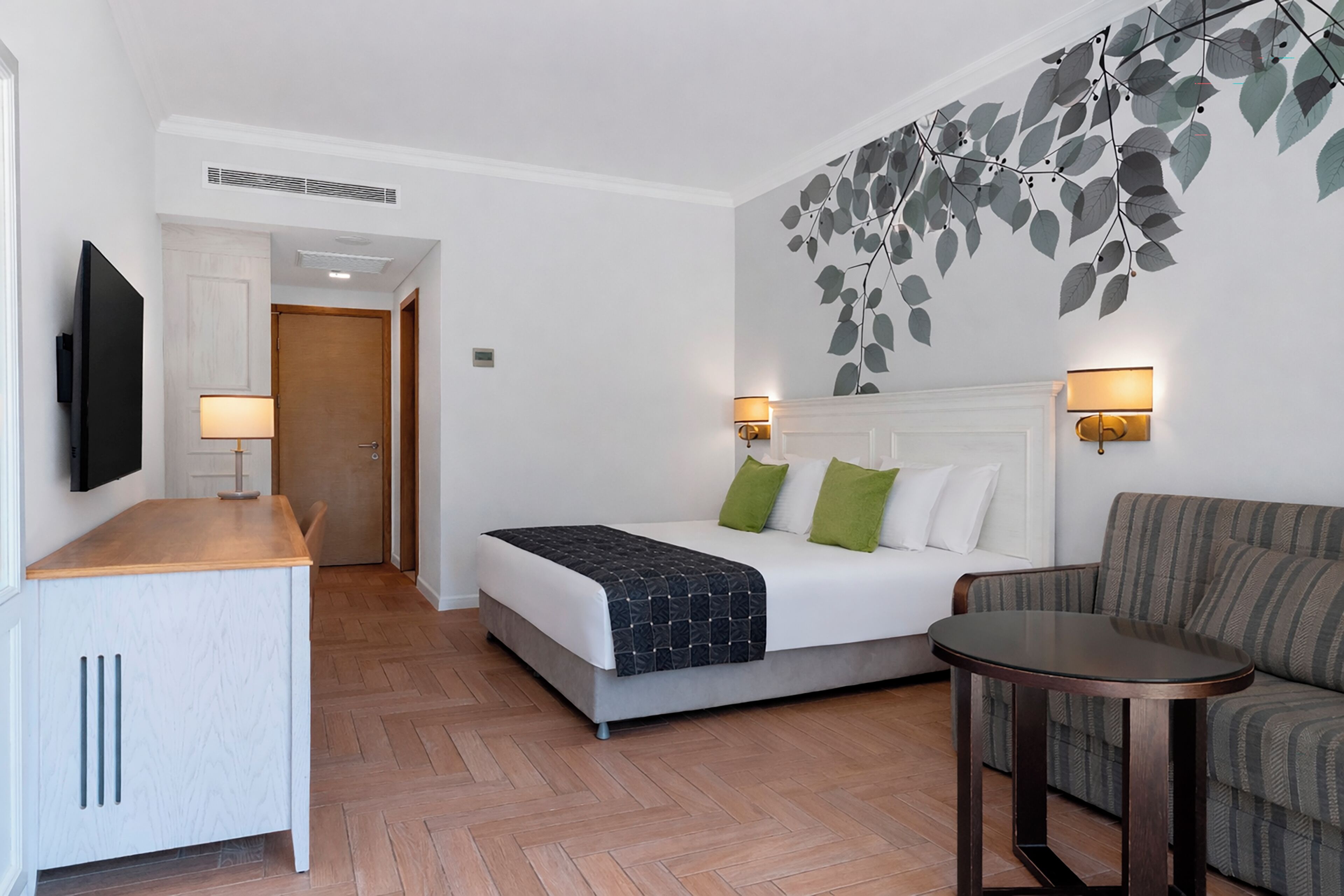 Ett hotellrum med en säng, en soffa, ett litet bord, en tv och en vägglampa.