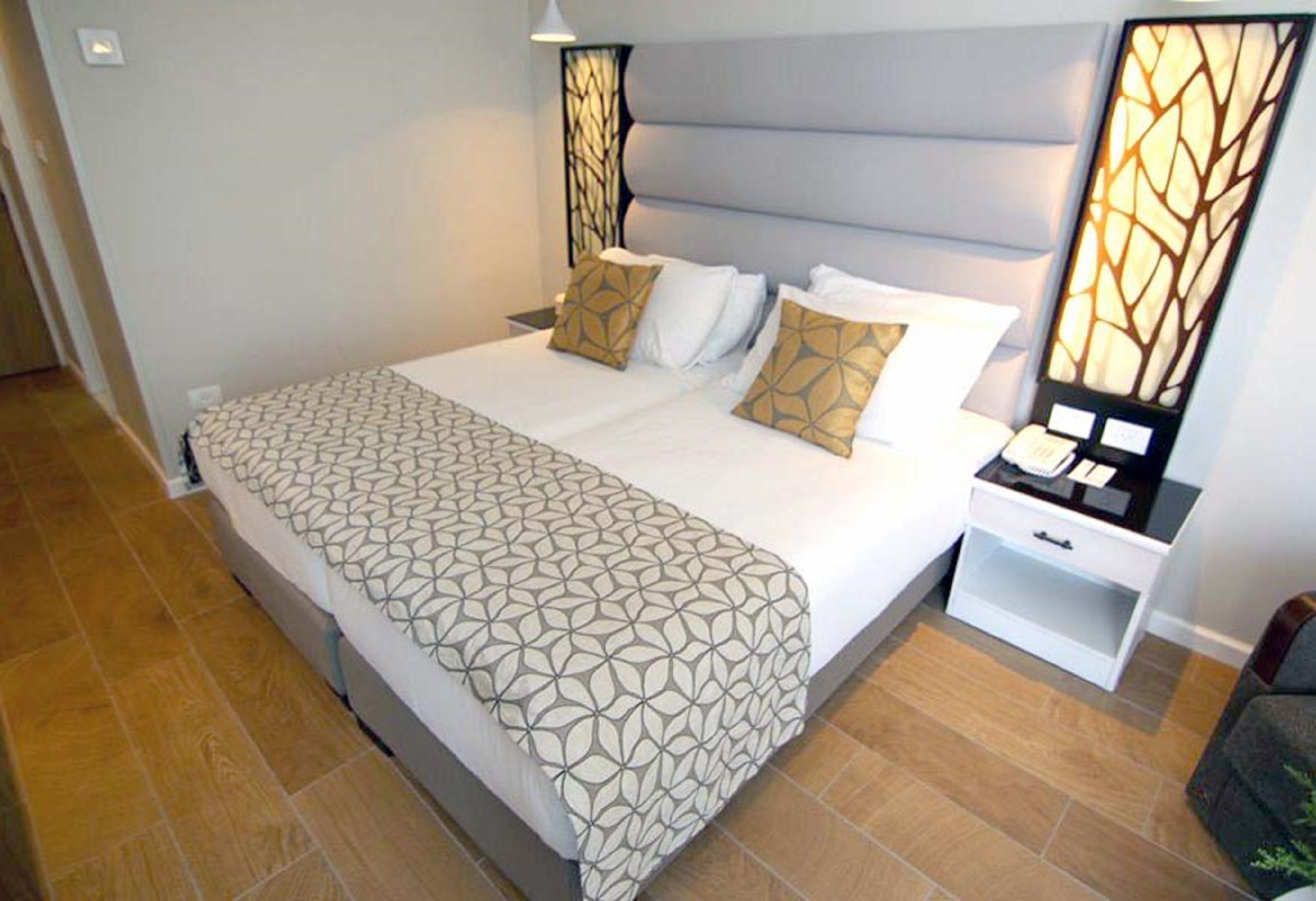 A neatly made bed with a geometric patterned bedspread, a headboard with a light fixture, and a bedside table with a lamp.