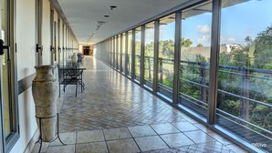 A corridor with large windows, a tiled floor, and a vase on the left.