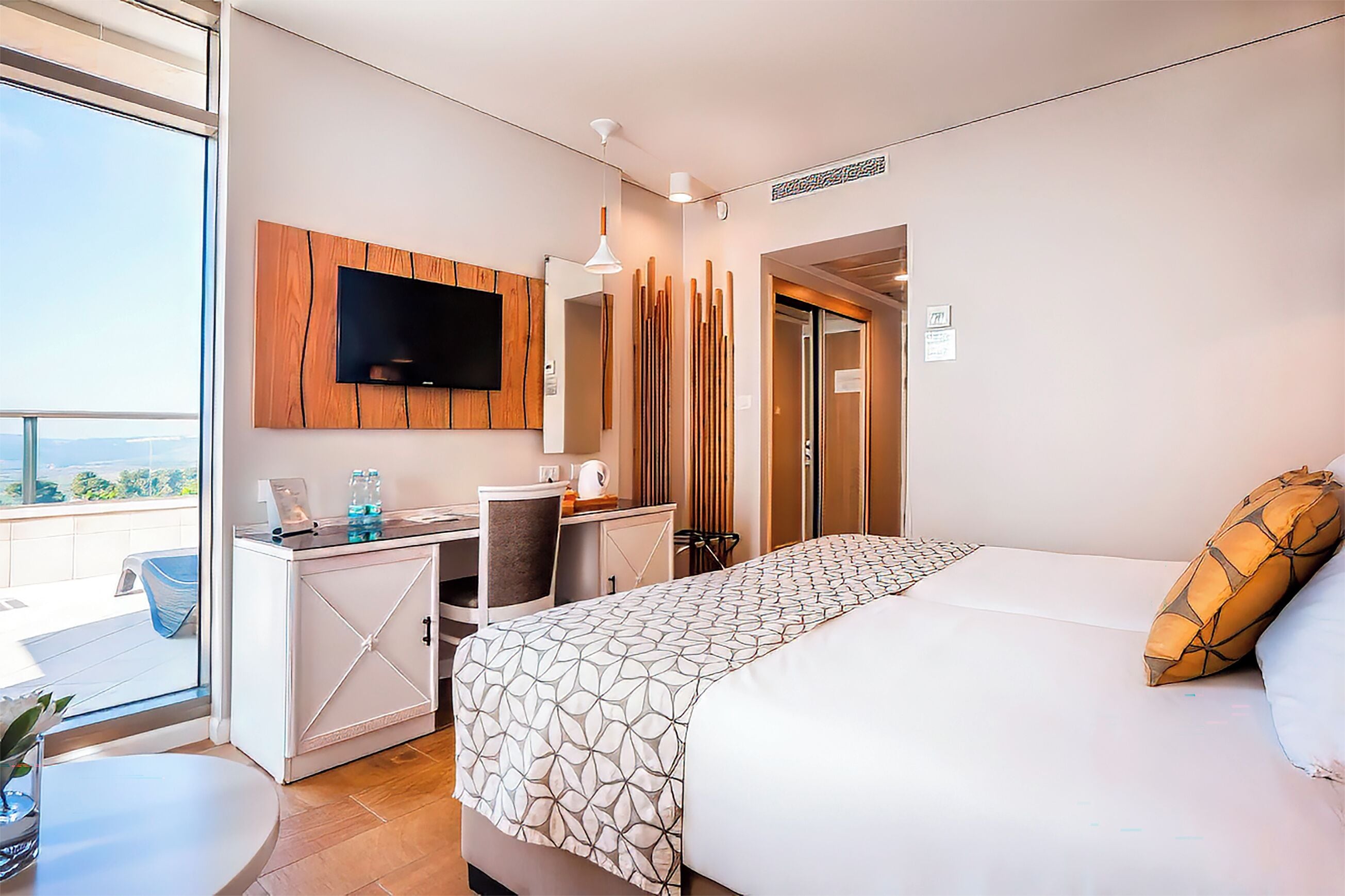 Une chambre d’hôtel avec un lit, un bureau, une télévision et un balcon offrant une vue.