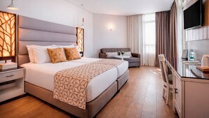 A modern hotel room with a large bed, a sofa, a TV, and a desk with a chair.