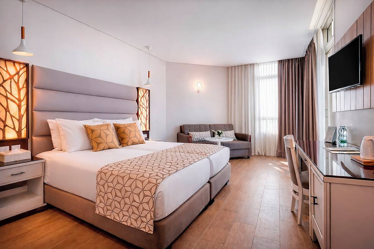 Ein modernes Hotelzimmer mit einem großen Bett, einer Sitzecke, einem Fernseher und einem Schreibtisch mit Stuhl.
