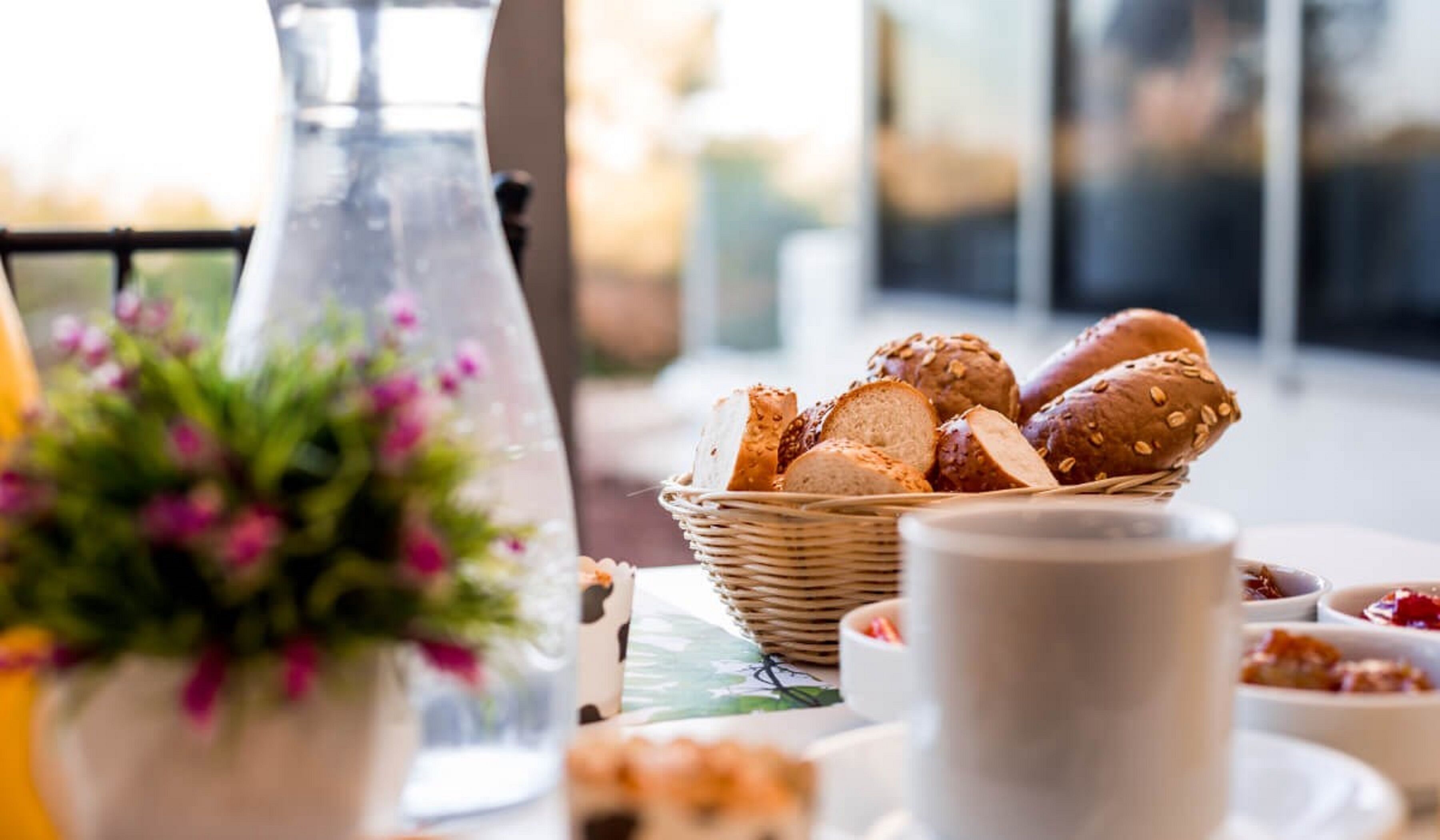 Een tafel met een mand vol sneetjes brood en een waterkan.
