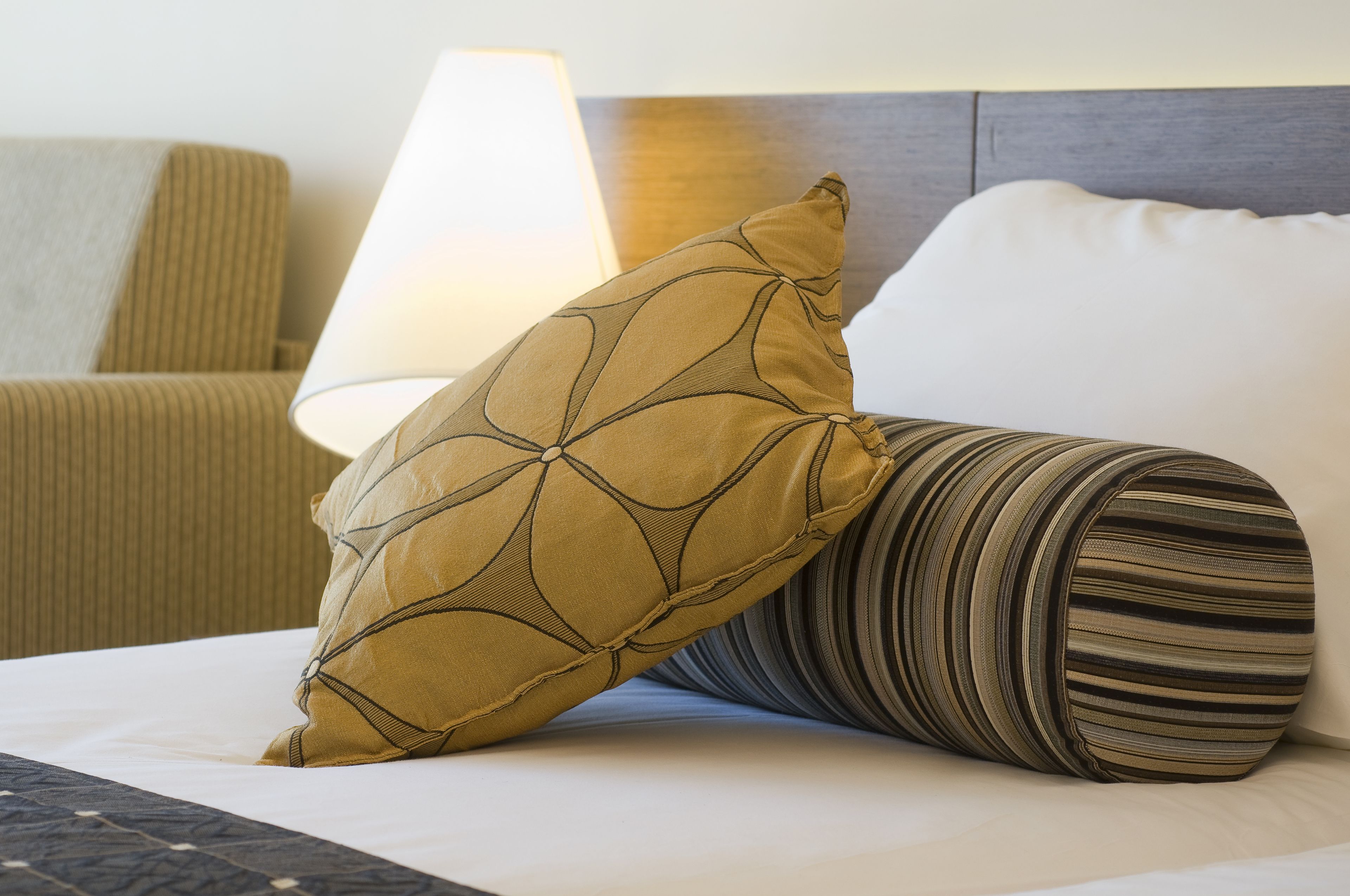 A bed with a patterned pillow and a striped pillow, a lamp, and a headboard.