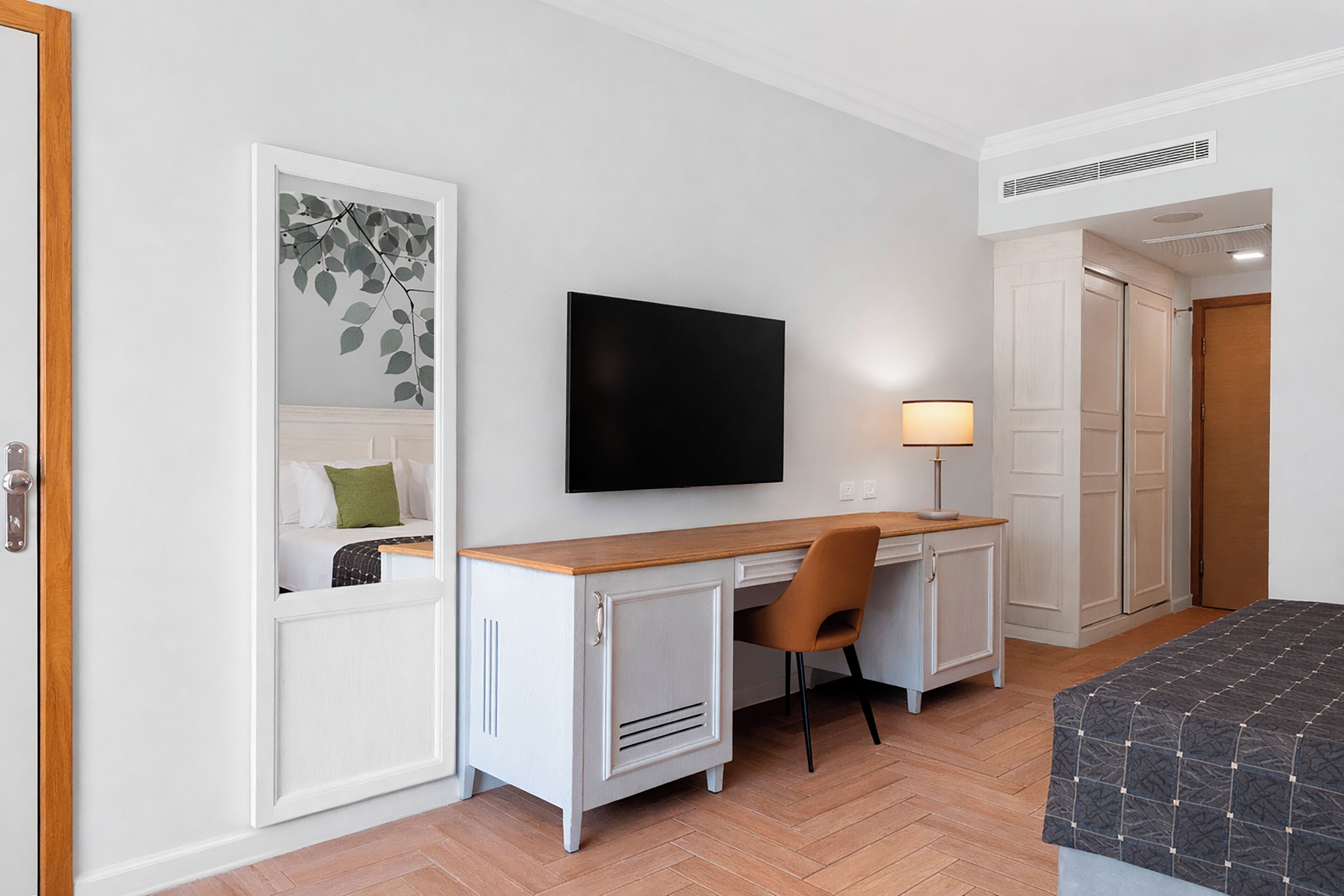 Et hotelværelse med seng, skrivebord med stol, fjernsyn og garderobeskab.