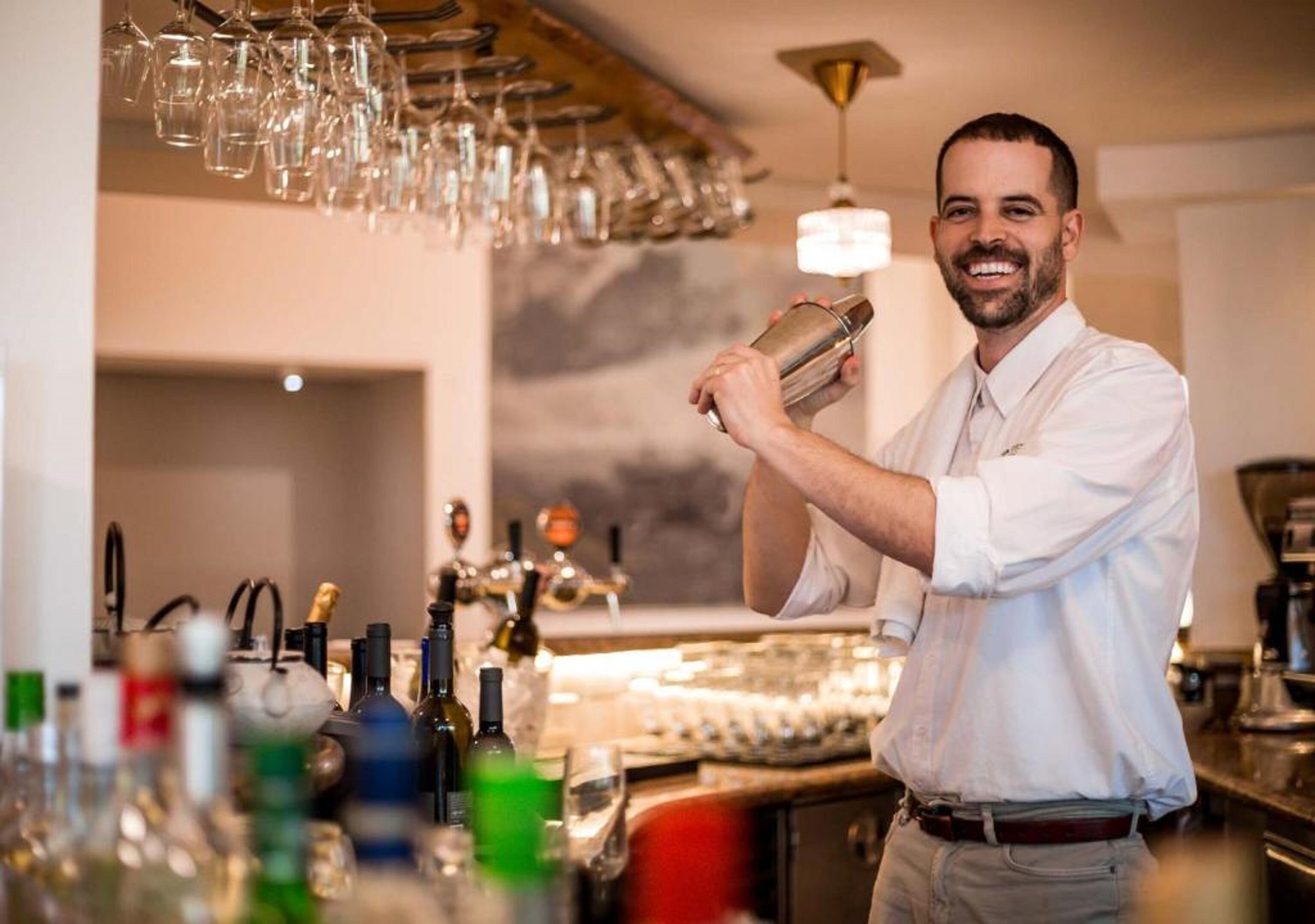 A bartender preparing a drink in a bar setting with a variety of bottles and glasses visible.