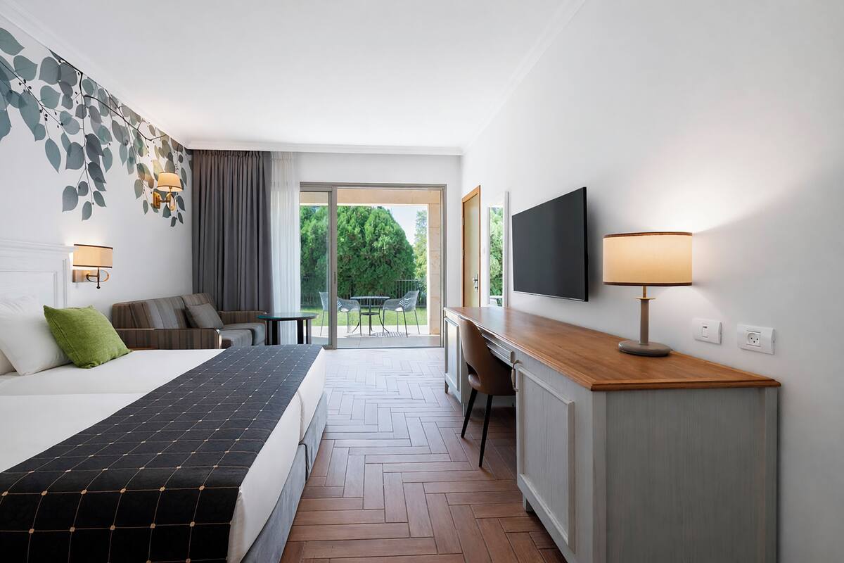 Ein Hotelzimmer mit Bett, Schreibtisch, Fernseher und Blick ins Freie.