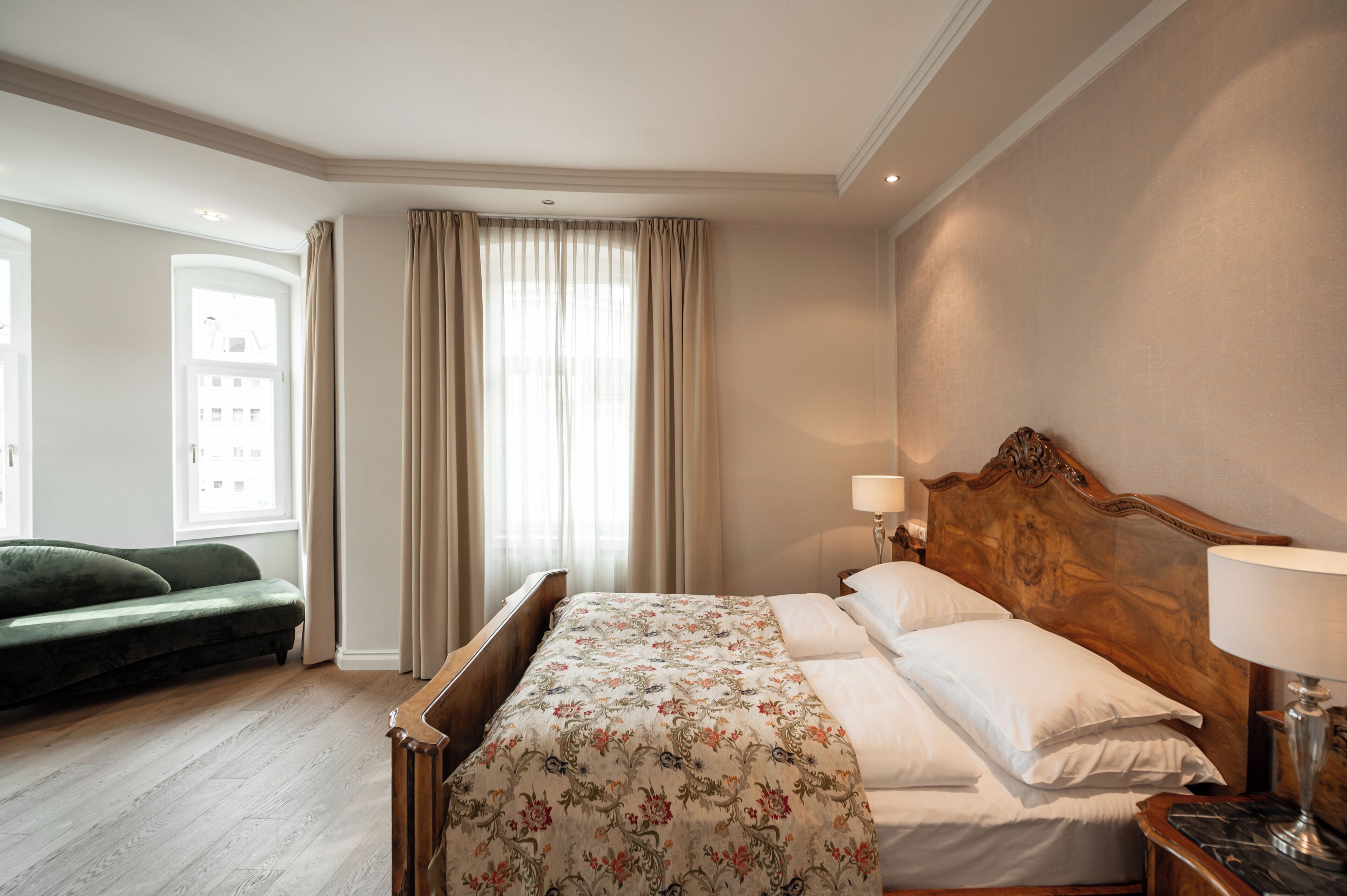 Una habitación de hotel con cama, mesita de noche, lámpara, sofá y ventana con cortinas.