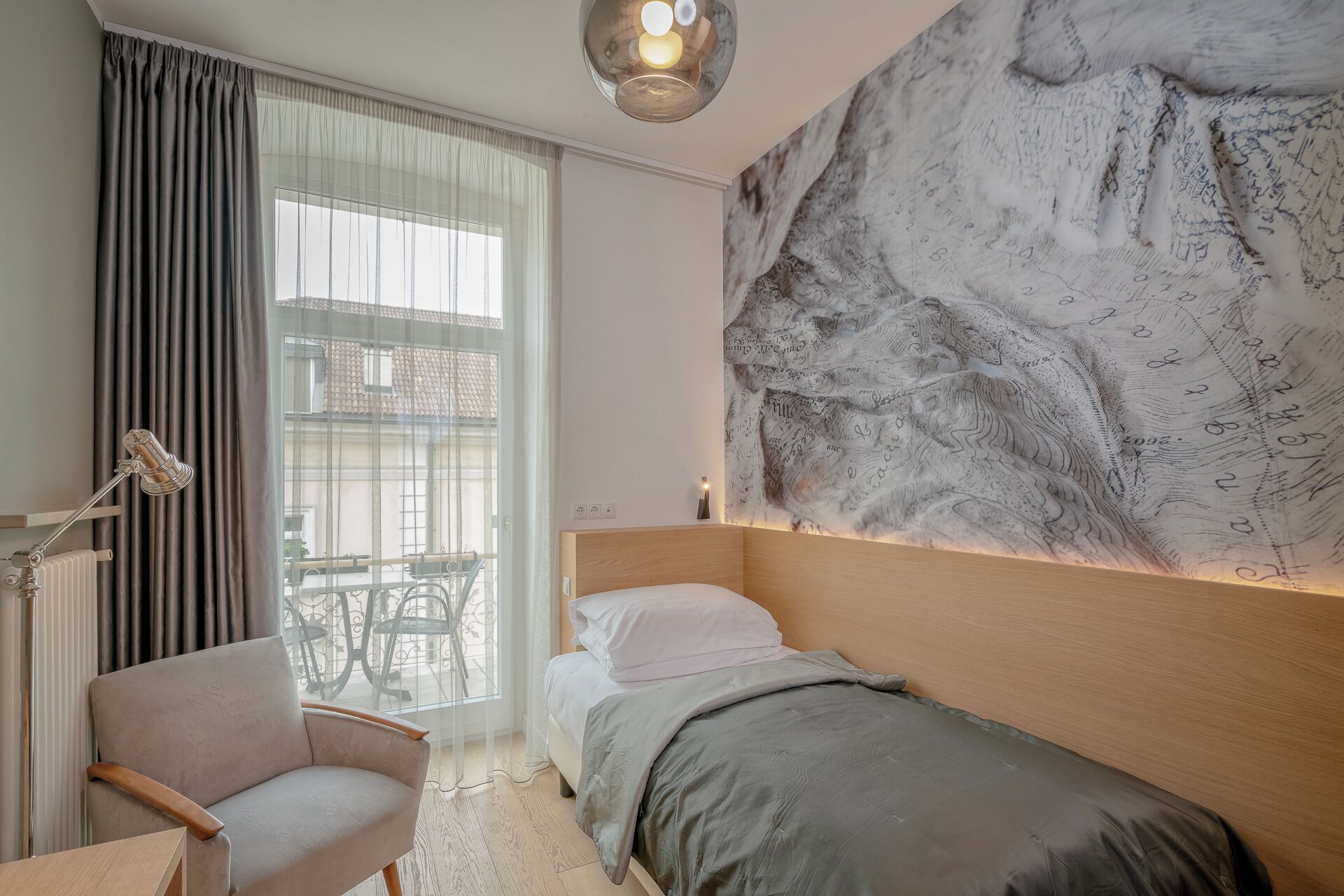 A bedroom with a bed, a chair, a desk, a large wall tapestry, and a window with curtains.