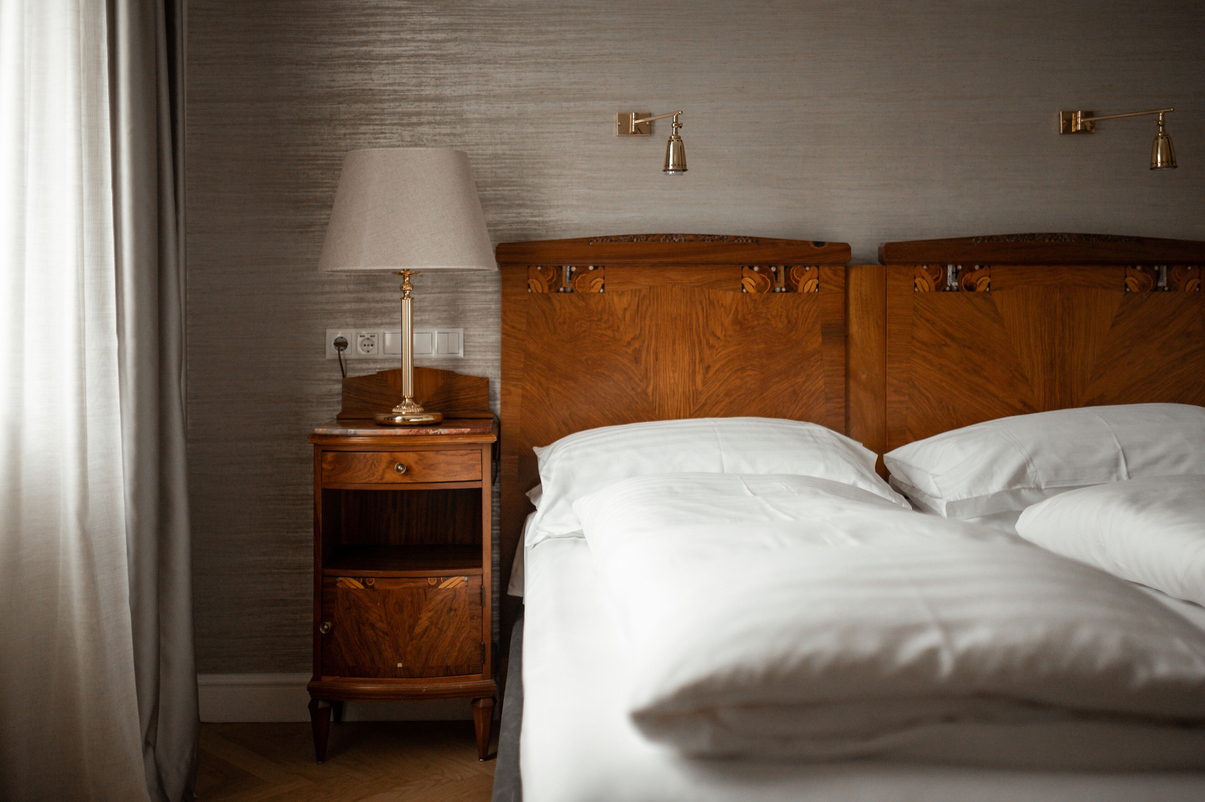 Una habitación de hotel con cabecera de madera, una mesita de noche con lámpara y cama con ropa blanca.