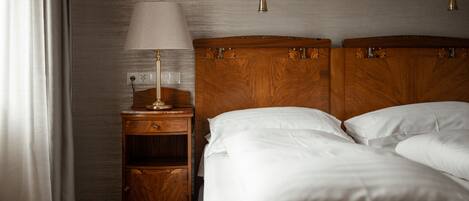 Una habitación de hotel con cabecera de madera, una mesita de noche con lámpara y cama con ropa blanca.