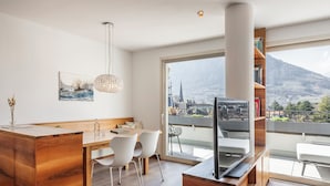Une cuisine moderne avec un coin repas, une grande fenêtre donnant sur la ville et un téléviseur posé sur un meuble en bois.