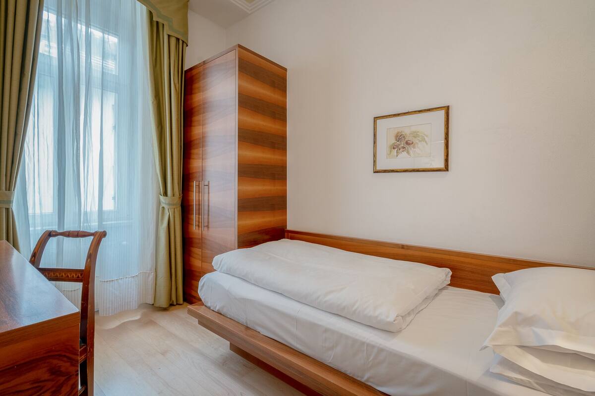 A hotel room with a bed, a wooden wardrobe, a desk, and a chair.