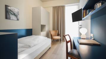 Ein Hotelzimmer mit Bett, Schreibtisch, Stuhl, Fernseher und Bücherregal.