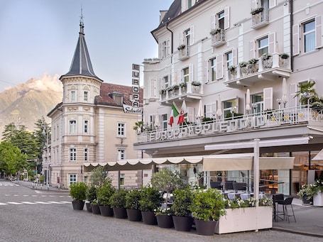 A hotel with a balcony, potted plants, and flags.