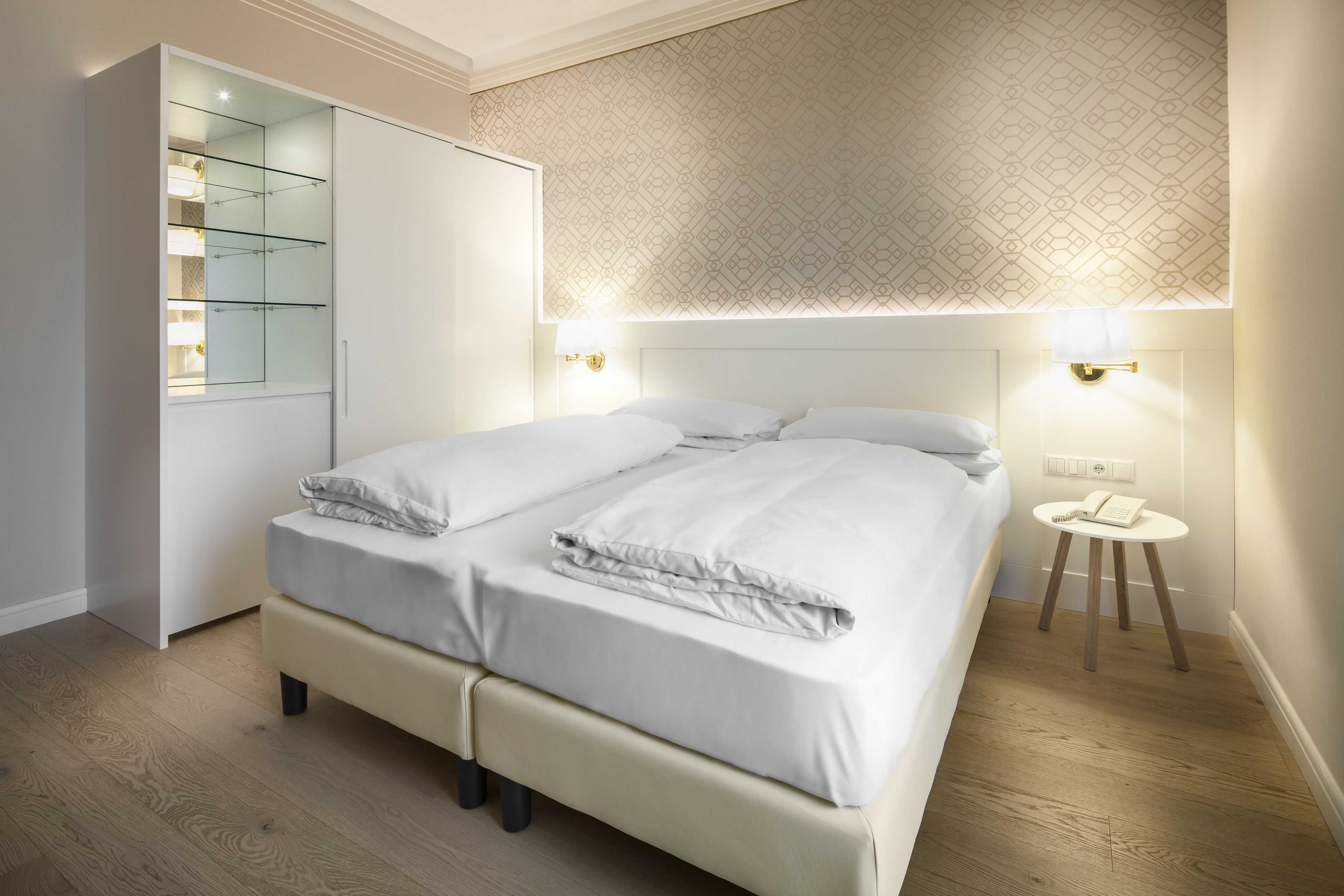 A modern bedroom with a large bed, a wardrobe, and a bedside table with a lamp.
