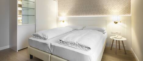 A modern bedroom with a large bed, a wardrobe, and a bedside table with a lamp.