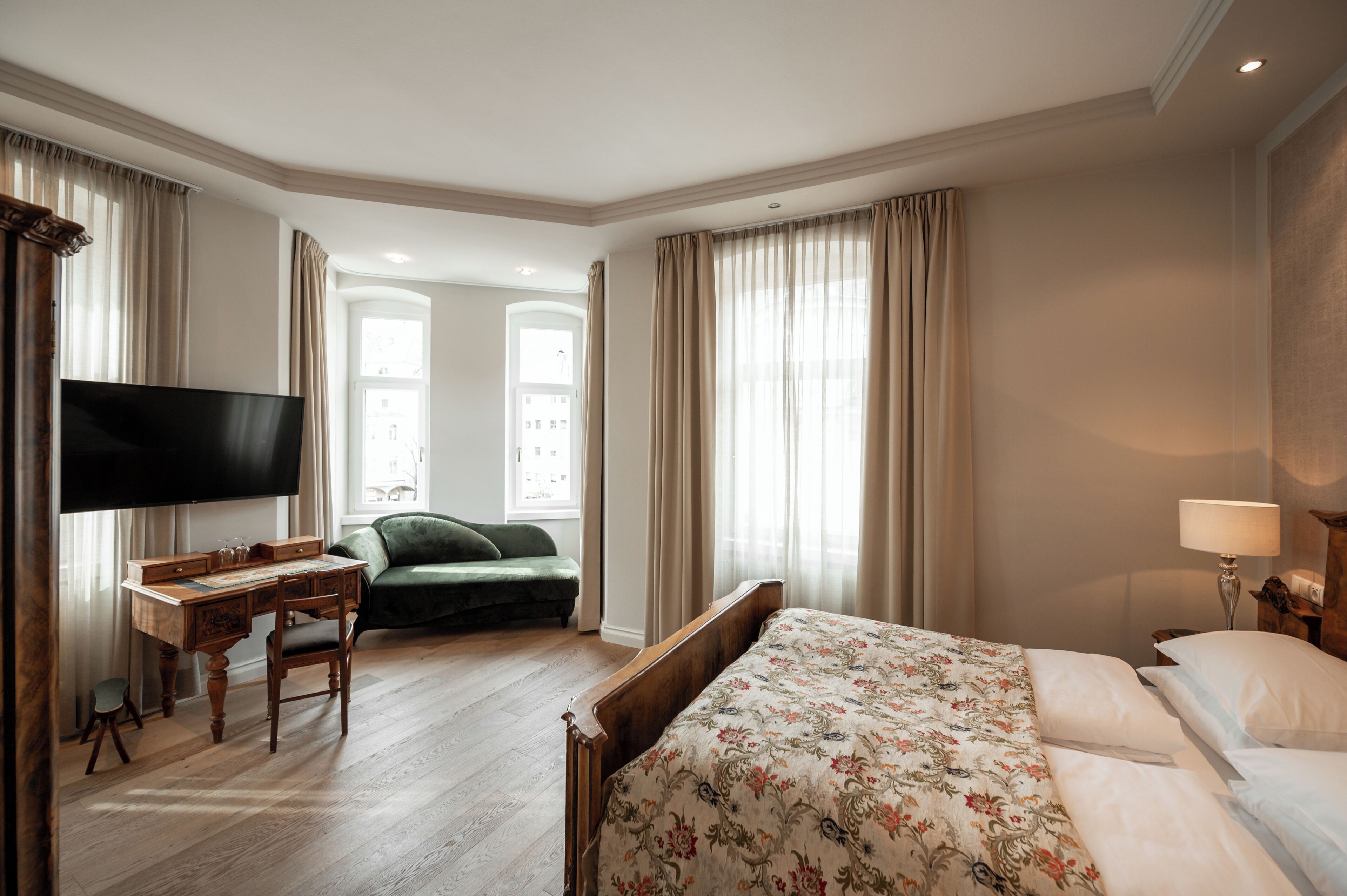 A hotel room with a bed, a desk with a television, a green sofa, and a lamp.