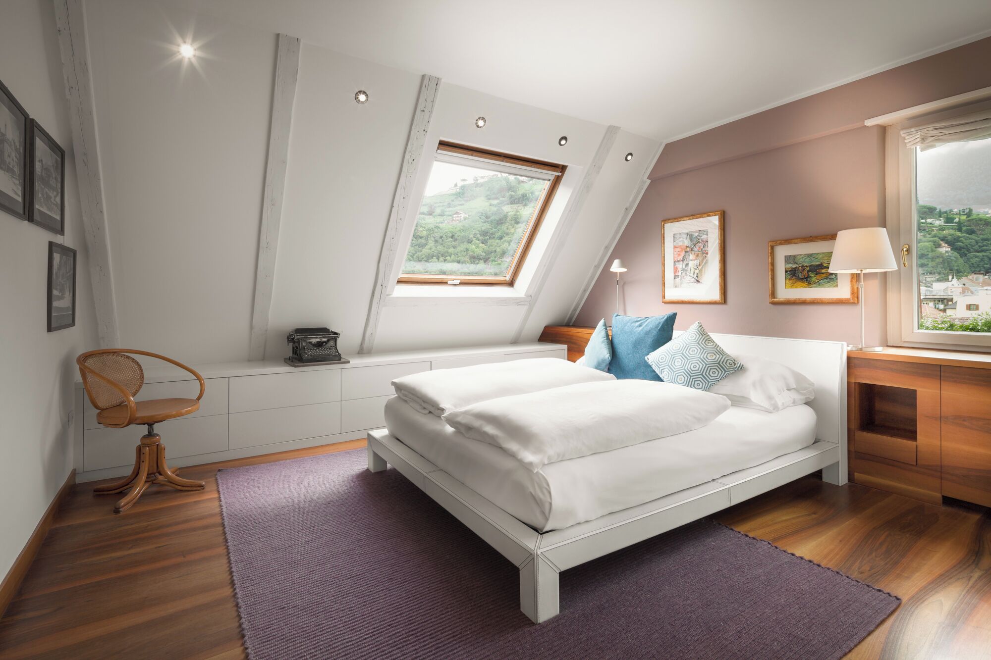 Ein Schlafzimmer mit Bett, Schreibtisch, Stuhl, Fenster und Blick ins Grüne.