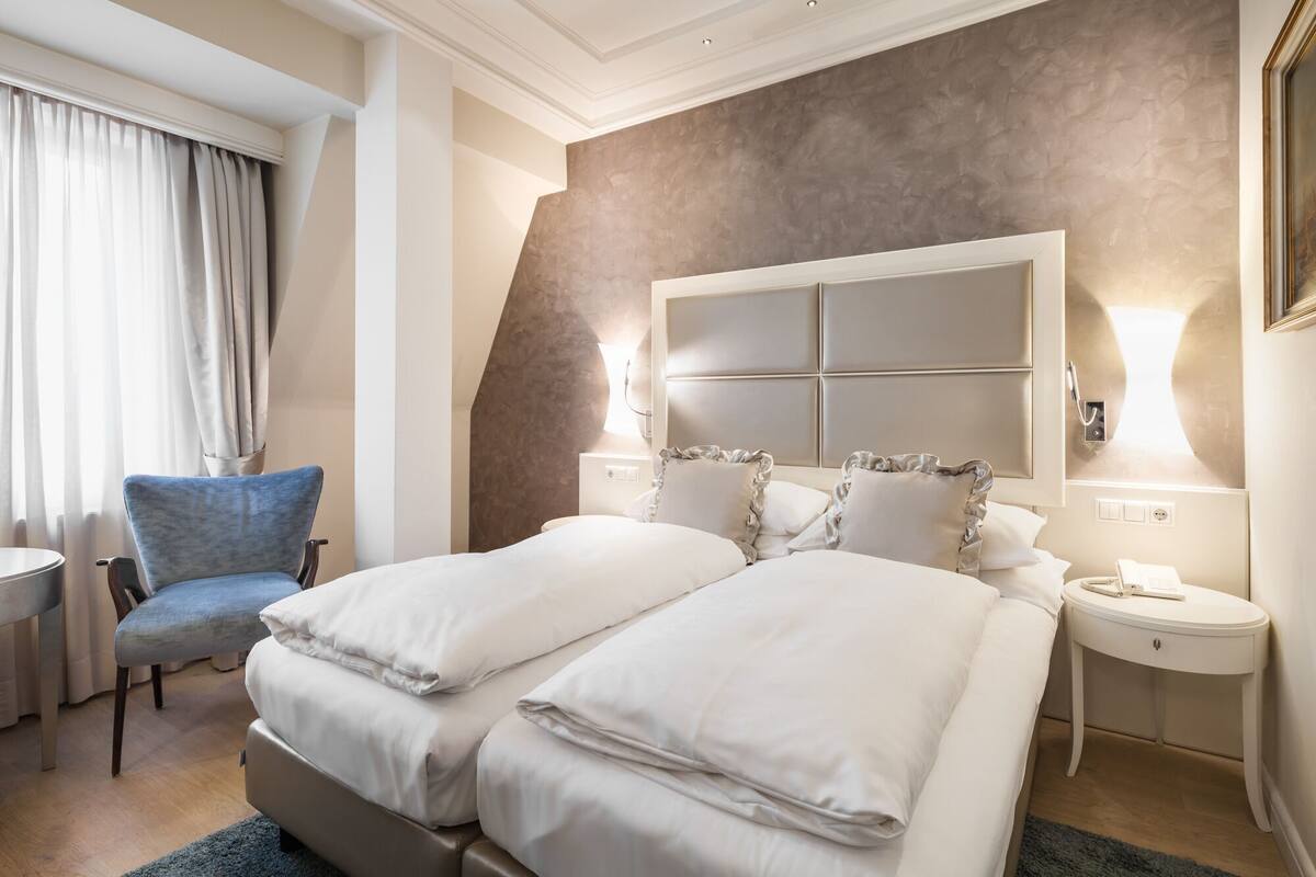 Habitación de hotel con cama doble, una silla, una mesita de noche y un tocador.