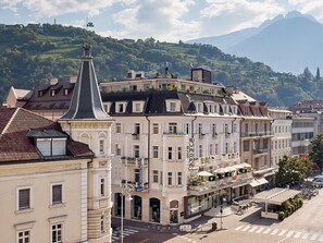 A historic building with a prominent tower, a ground-level entrance, and a balcony with potted plants. - Hotel Europa Splendid (Merano)
