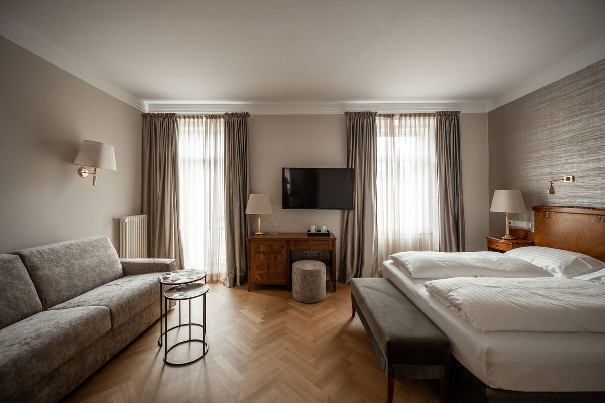 A hotel room with a sofa, a bed, a desk with a flat-screen TV, and a lamp.