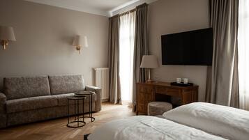 Ein Hotelzimmer mit Sofa, einem kleinen Tisch, einem Schreibtisch mit Lampe, Fernseher und Bett.