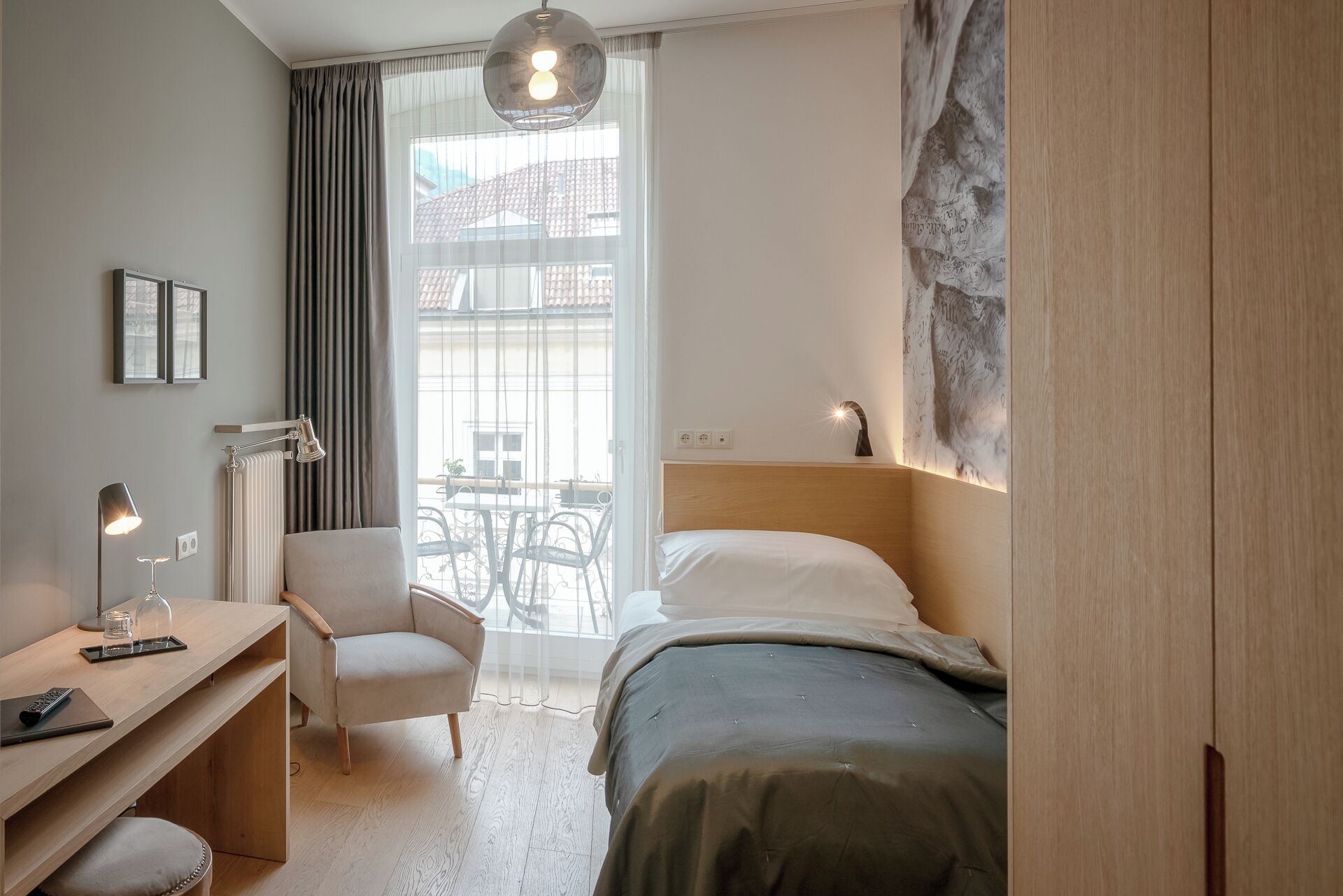 A bedroom with a bed, a desk, a chair, a radiator, and a window with curtains.