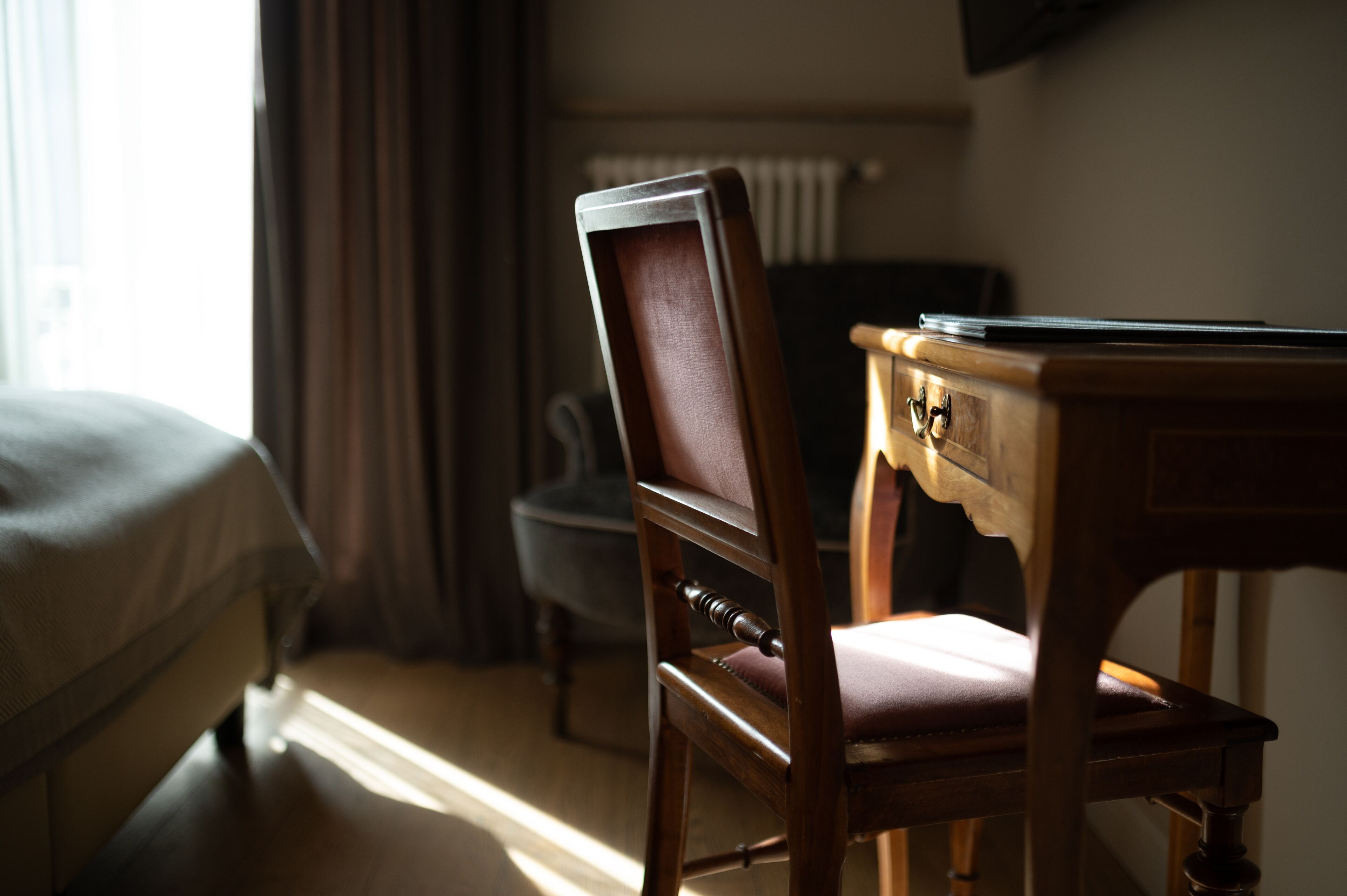 Una habitación de hotel con un escritorio de madera, una silla, una cama y un radiador.